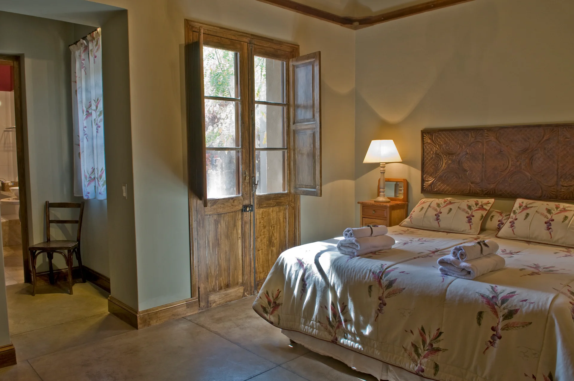 Standard room with elegant decor, natural light, and antique wooden doors opening to the outdoor patio at Verde Oliva in Maipú Mendoza